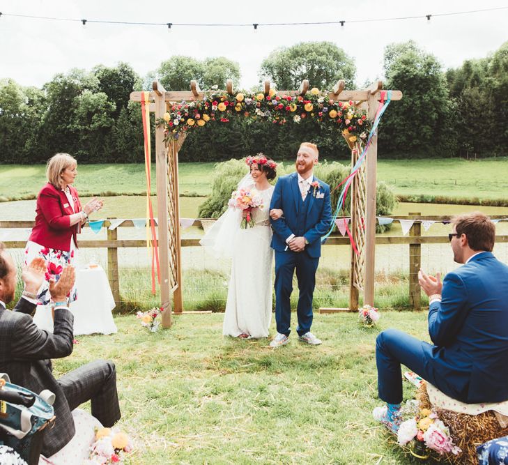 Wedding Ceremony | Bride in Lace Watters Gown &amp; Colourful Flower Crown | Groom in Navy Suit | Bright Festival Themed Outdoor Ceremony &amp; Tipi Weeding |  Maryanne Weddings | Framed Beauty Film