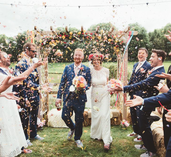 Confetti Exit | Bride in Lace Watters Gown &amp; Colourful Flower Crown | Groom in Navy Suit | Bright Festival Themed Outdoor Ceremony &amp; Tipi Weeding |  Maryanne Weddings | Framed Beauty Film