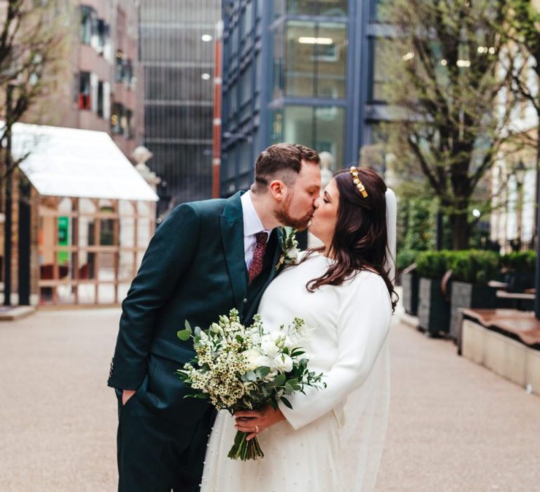 Bride and groom kiss at Devonshire Terrace wedding wearing two piece dress and white floral bouquet