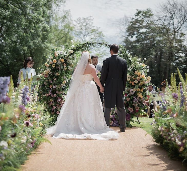 Bride in Lace Sophia Tolli Wedding Dress and Groom in Traditional Tails Exchanging Vows During the Outdoor Wedding Ceremony