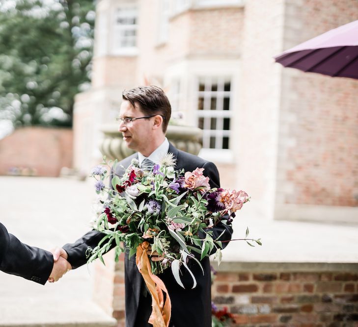 Groom in Traditional Morning Suit Holding the Brides Oversized Wedding Bouquet