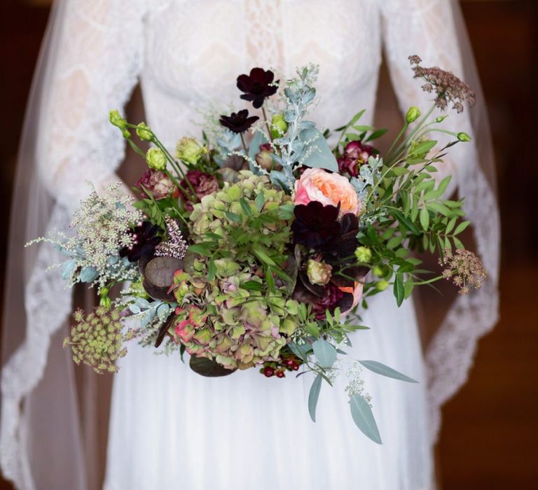 Bride in Lace Lihi Hod Sophia Wedding Dress Holding a Green and Red Winter Wedding Bouquet