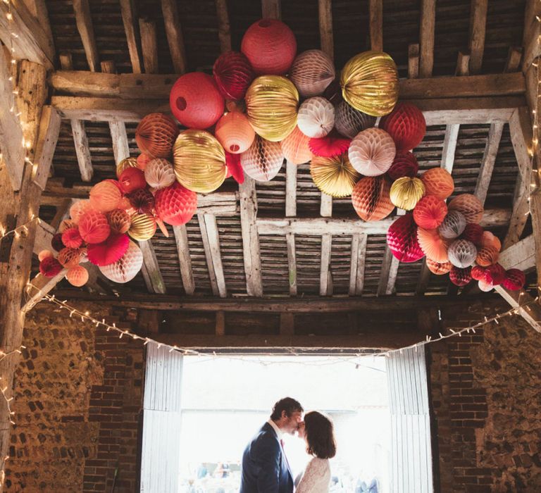 Bride in Lace Wedding Dress from Hope &amp; Harlequin and Groom in Navy Hugo Boss Suit Standing under Pom Pom Wedding Decor