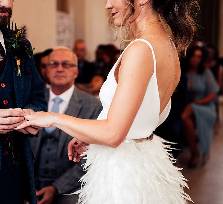 Bride in Charlie Brear Payton Bridal Gown &amp; Piora Feather Skirt and Groom in Three Piece Wool Suit Exchanging Vows