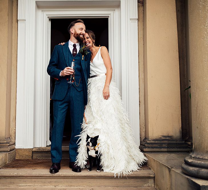 Bride in Charlie Brear Payton Bridal Gown &amp; Piora Feather Skirt and Groom in Three-piece Wool Suit with Their Pet Pug