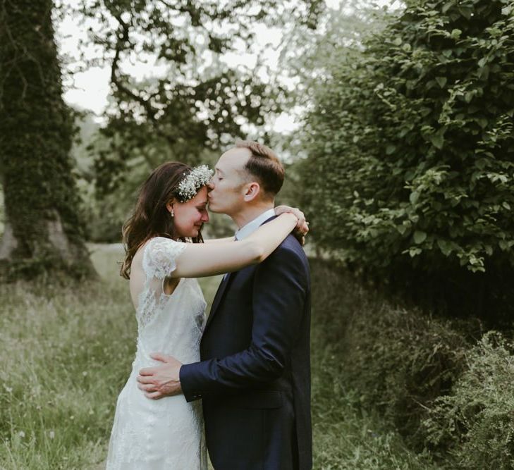 Groom kisses bride who wears lace dress and flower crown