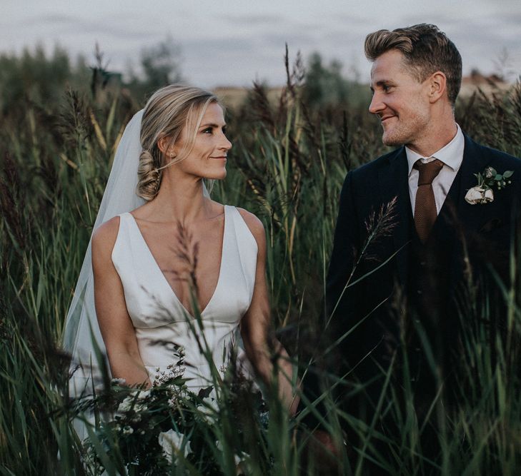 Bride in Jesus Peiro Wedding Dress and Groom in Navy Suit Standing in the Fields