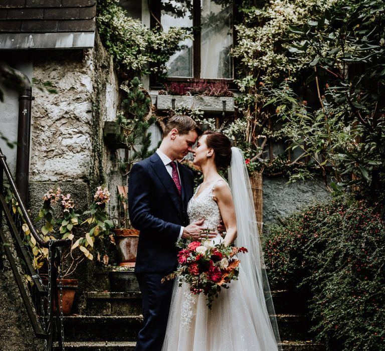 Bride in Lace Angelic Bridal Gown and Groom in Navy Suit Embracing