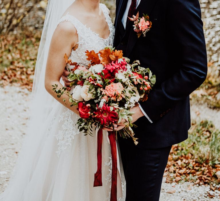 Bride and Groom Embracing Holding a Red, Orange and Green Wedding Bouquet with Ribbons