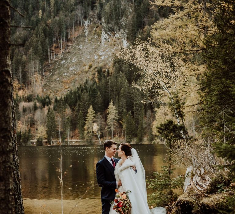 Bride in Long Cover Up Standing With Her Groom by The Waters Edge in Hallstatt, Austria