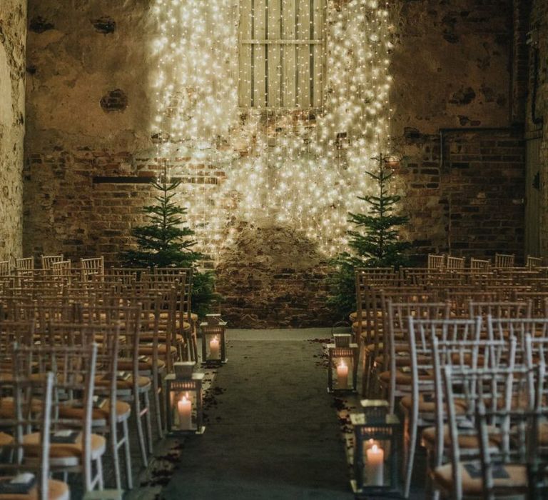 Fairy light curtain for New Years eve ceremony in a barn with Christmas trees and lantern aisle decor