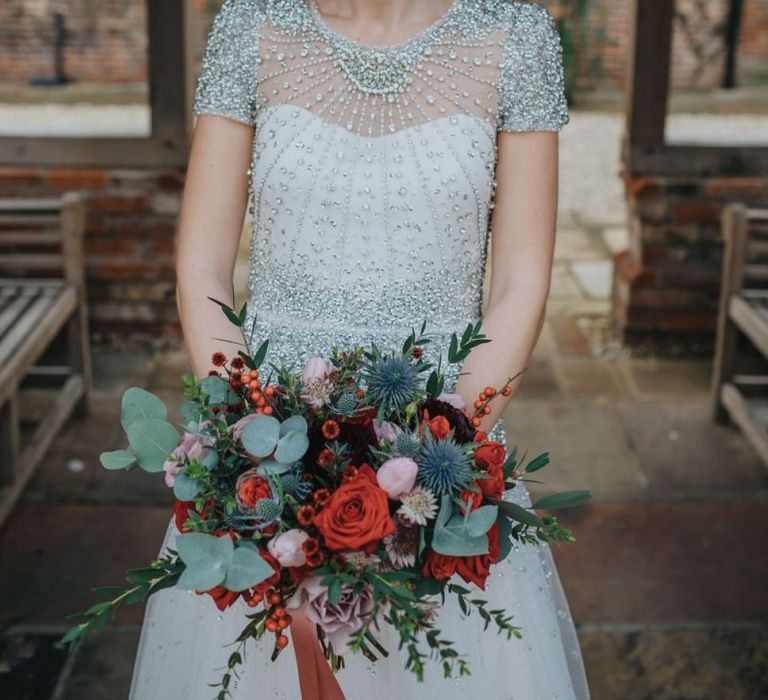 Close up detail of brides embellished wedding dress teamed with a red lip and a festive floral bouquet