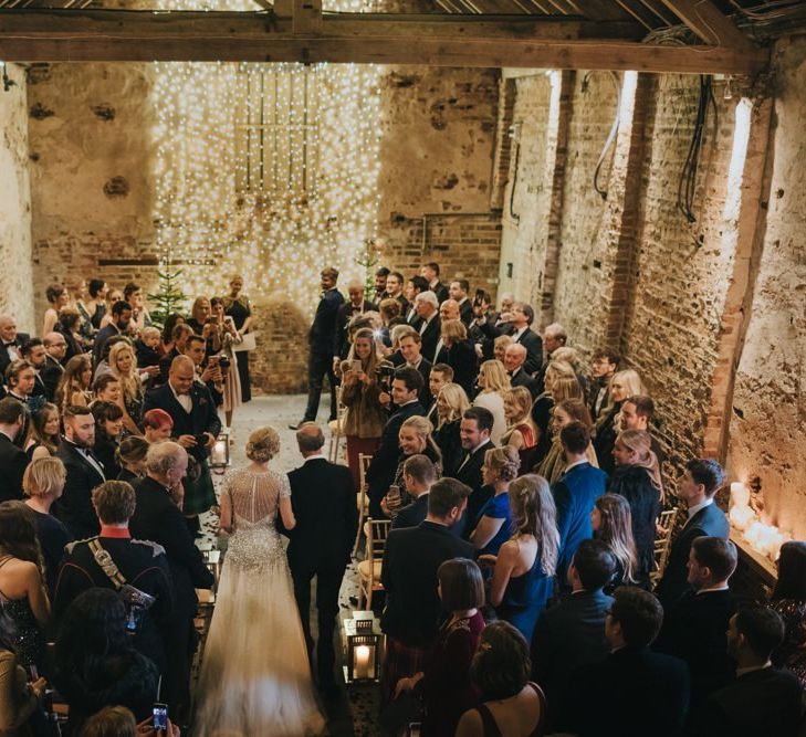 Winter ceremony with candle lantern aisle and a fairy light curtain with Christmas trees