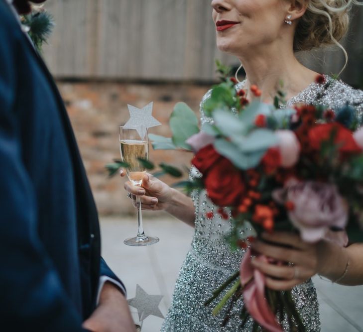 Bride and groom at winter styled wedding with red floral bouquet and a navy velvet suit