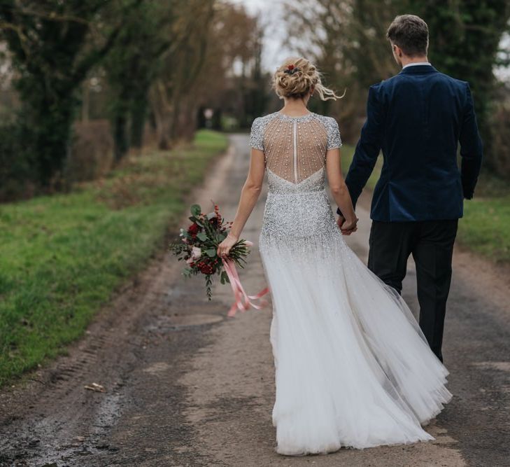 Back of brides embellished wedding dress with groom wearing a navy velvet suit at winter wedding