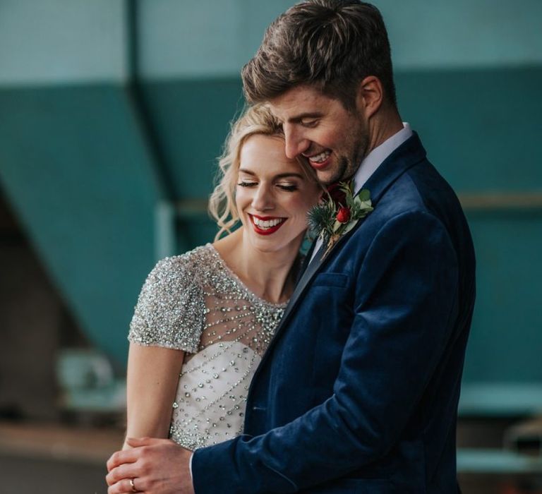 Bride and groom embrace at winter wedding wearing an embellished wedding dress and navy velvet suit