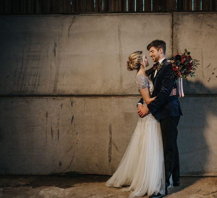 Bride and groom embrace at winter wedding wearing an embellished wedding dress and navy velvet suit