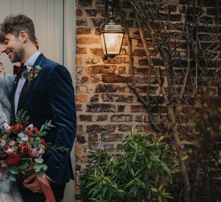 Bride and groom embrace at winter wedding wearing an embellished wedding dress and blue bridal jacket