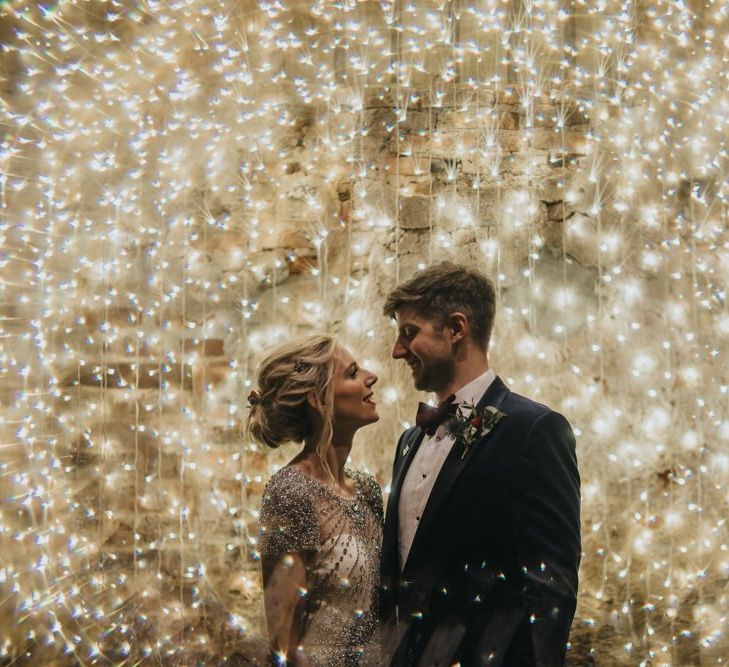 Bride and groom embrace with fairy light curtain at New Years eve wedding