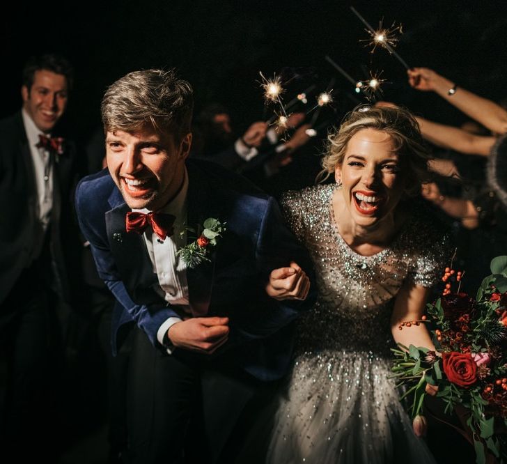 Bride and groom confetti exit wearing embellished wedding dress and red rose floral bouquet