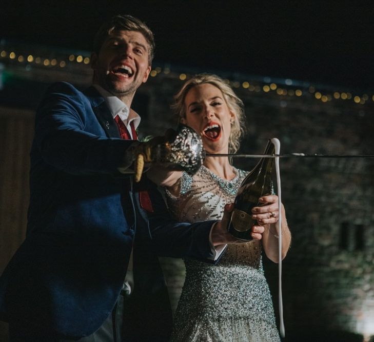 Bride and groom using a sword to open a bottle of champagne at winter reception