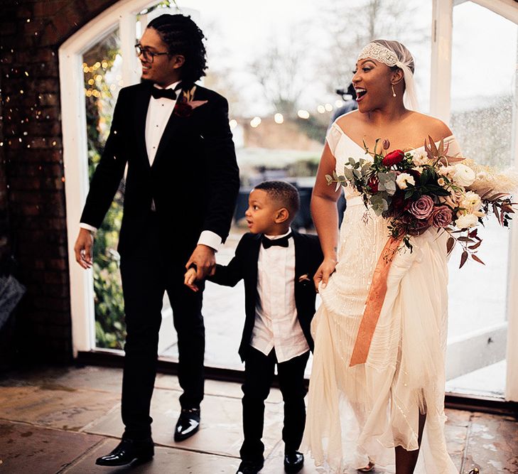 Black Bride in Juliet Cap Veil and Eliza Jane Howell Wedding Dress and Groom in Tuxedo Entering The Wedding Breakfast with Their Page Boy