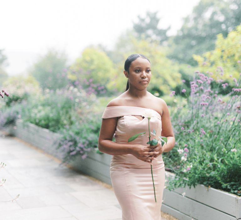 Bridesmaid in off the shoulder pastel dress holding a single flower stem