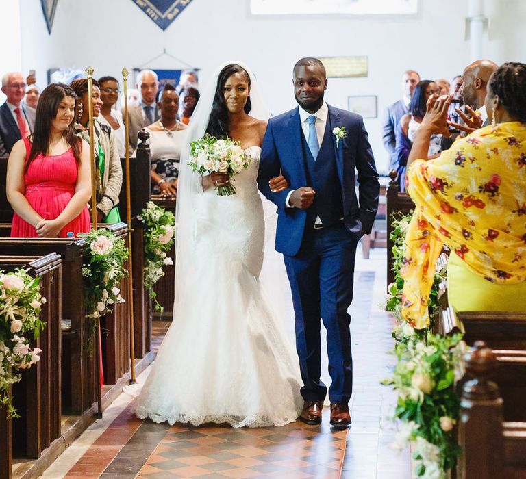 Bride in Lace Fishtail Gown with Strapless Sweetheart Neckline by Suzanne Neville | Lace Edged Cathedral Length Veil | Bridal Bouquet of White and Blush Roses and Peonies | Groomsman in Blue Three-Piece Ted Baker Suit | Rose and Peony Pew Ends | Wedding Ceremony at St John the Baptist Church, Elmore | Peg Board Table Plan &amp; DIY Sweet Table for an Elmore Court Wedding | Mavric Photography