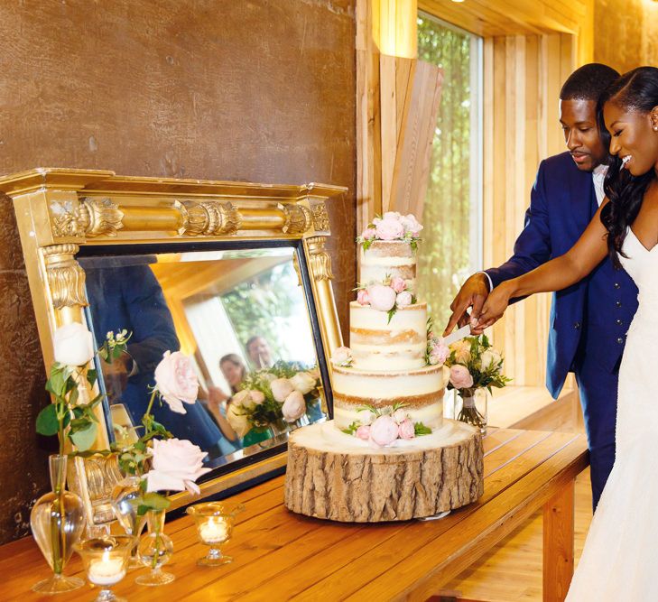 Bride in Lace Fishtail Gown with Strapless Sweetheart Neckline by Suzanne Neville | Groom in Blue Three-Piece Ted Baker Suit with Blush Pink Tie | Three-Tier Semi-Naked Wedding Cake | Log Slice Cake Stand | Gold Mirror | Peg Board Table Plan &amp; DIY Sweet Table for an Elmore Court Wedding | Mavric Photography