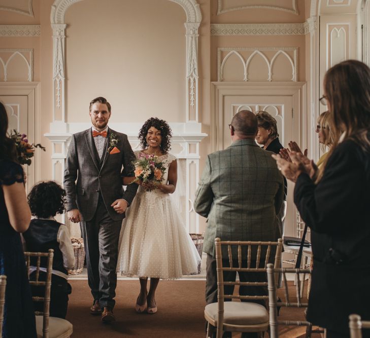 Bride in Polka Dot Tulle Short Wedding Dress  and Groom in Grey Check Suit Walking up the Aisle Just Married