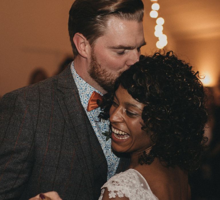 Groom in Wool Suit, Floral Shirt and Bow Tie Kissing His Brides Head During the First Dance