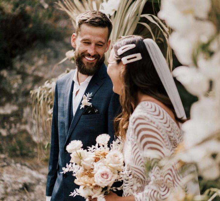 Groom in Moss Bros. Navy Wedding Suit and Bride in Margaux Tardits Wedding Dress Laughing During the Wedding Ceremony