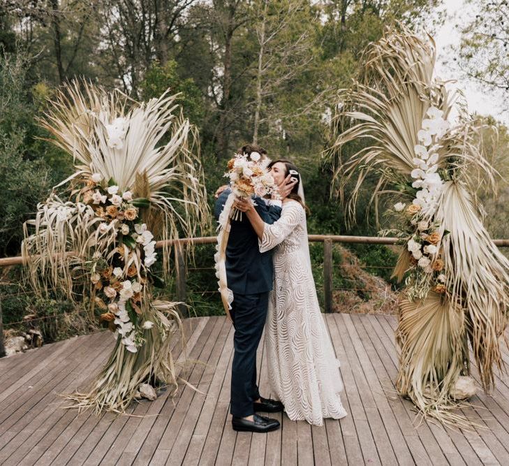 Bride in Margaux Tardits Wedding Dress  and Groom in a Navy Wedding Suit  Kissing at the Altar