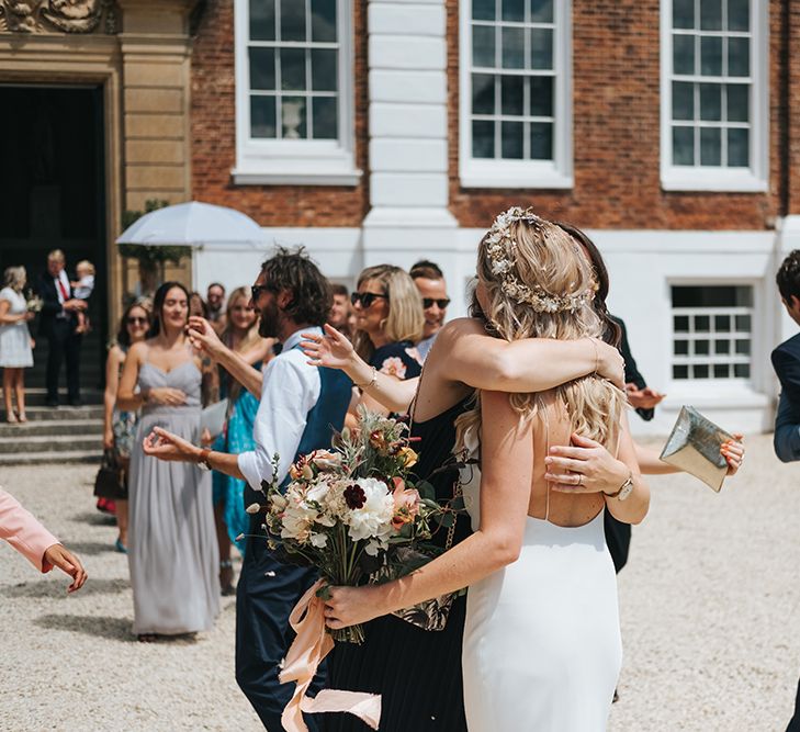 Wedding Guests Embracing the Bride in a Spaghetti Strap Savannah Miller Wedding Dress and Flower Crown