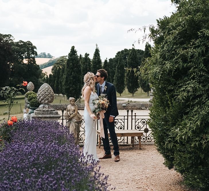 Bride in Fitted Savannah Miller Chloe Wedding Dress and Flower Crown Kissing Her Groom in the Pynes House Gardens