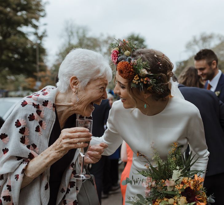 Bride in Satin Wedding Dress with Autumnal Flower Crown Talking to Wedding Guest