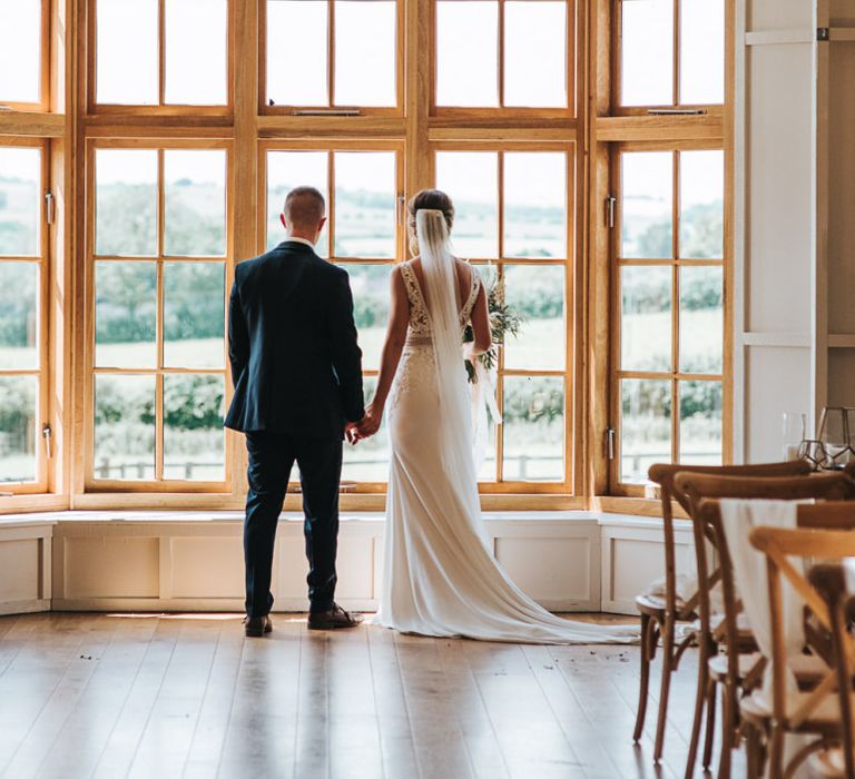 Bride and Groom Look Out Of Venue Holding Hands