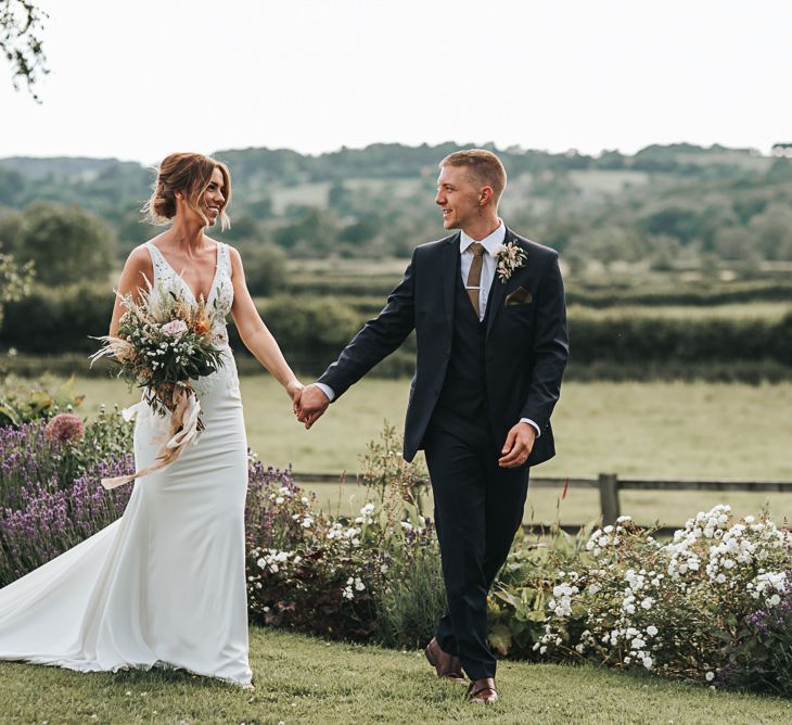 Bride and Groom Walk Hand In Hand In Venue Grounds