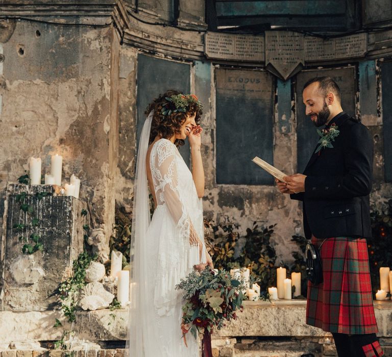 Emotional Bride in a Boho Rue De Seine Wedding Dress Wiping Her Tears as Her Groom in Red Tartan Kilt Reads His Wedding Vows