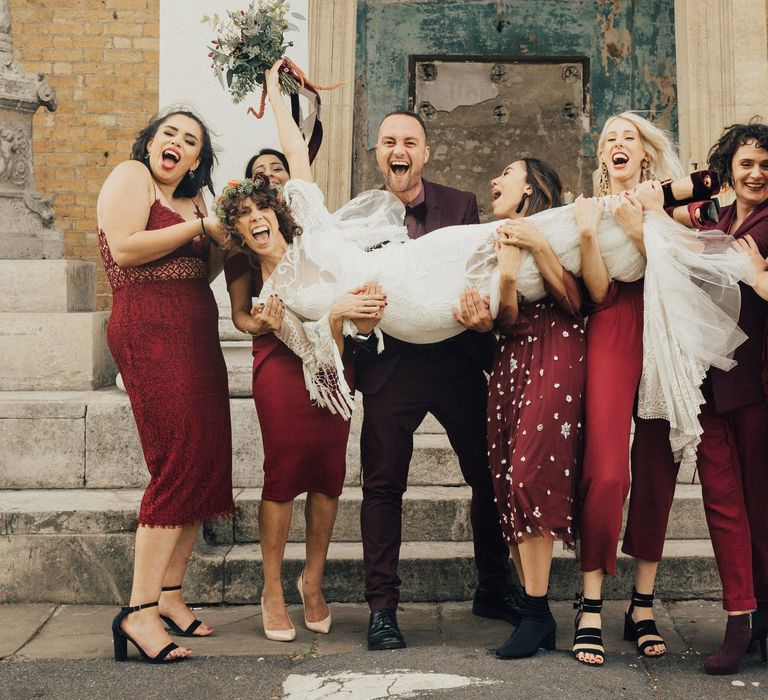 Bridal Party in Different High Street Burgundy Outfits Holding the Bride in a Rue De Seine Boho Wedding Dress