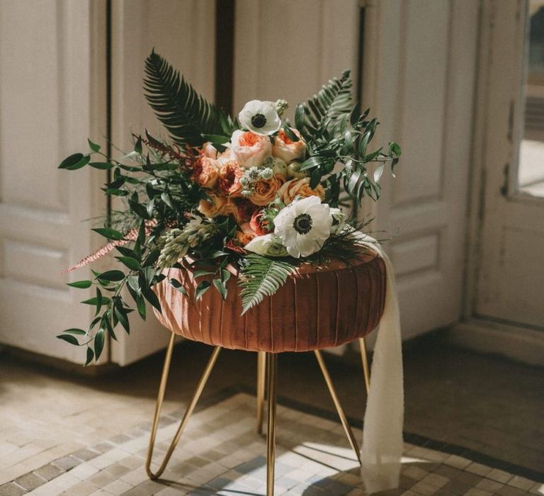 Romantic Bouquet with Anemones and Fern Tied with Ribbon Sitting on a Velvet Stool