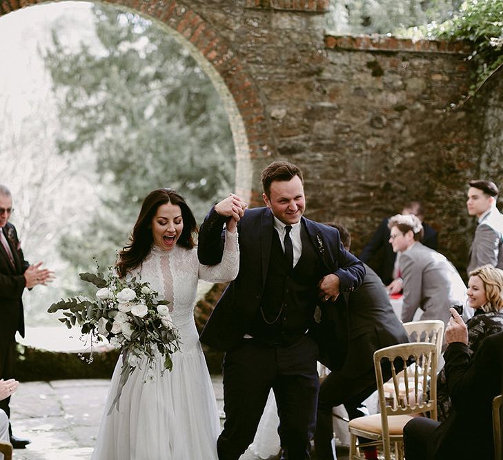 Bride in a Homemade Wedding Dress with Lace Bodice and Long Sleeves and Groom in Navy Suit Walking Up the Aisle