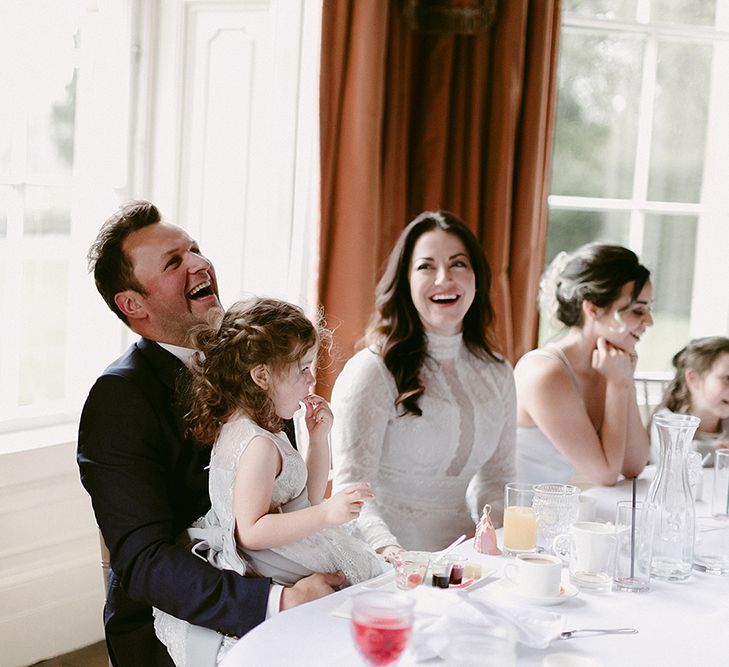 Bride in Homemade Wedding Dress with High Neck and Long Sleeves Laughing During The Speeches with Her Groom in Zara Suit