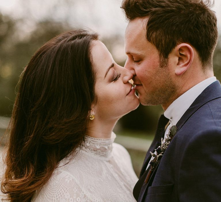 Bride in Homemade Wedding Dress with Lace Long Sleeves and High Neck and Groom in Navy Zara Suit Kissing