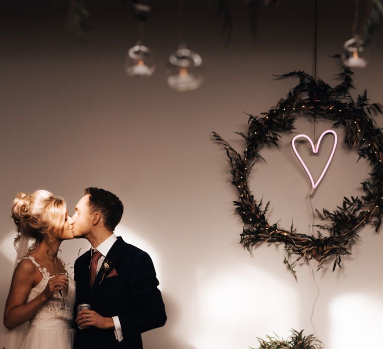 Bride and Groom Kissing with Neon Heart in Greenery Hoop