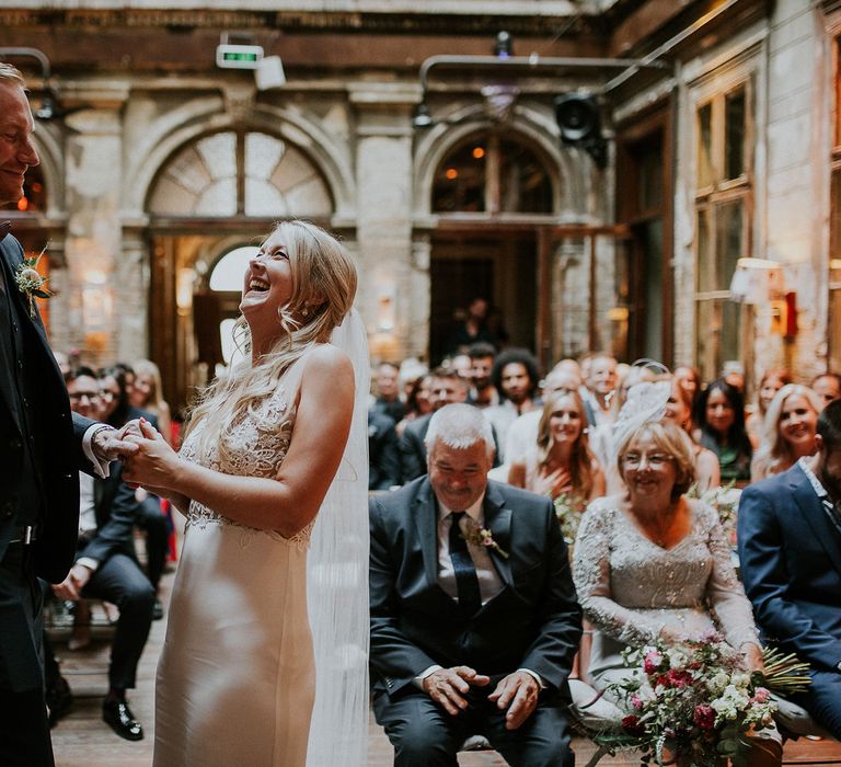 Bride in Lila Gown by Alexandra Grecco with Fitted Silk Crepe Skirt and Sheer Italian Tulle Bodice Covered in Floral Lace Applique | Theia Bridal Veil with Petal Detail | Groom in Black Three-Piece Suit from Hackett with Burgundy Bow Tie from Zara | Wedding Ceremony at Brody Studios | Budapest Wedding with Giant Bridal Bouquet, Tuk Tuks and Cadillac | Jágity Fanni Fotográfus