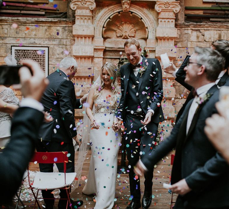 Bride in Lila Gown by Alexandra Grecco with Fitted Silk Crepe Skirt and Sheer Italian Tulle Bodice Covered in Floral Lace Applique | Theia Bridal Veil with Petal Detail | Groom in Black Three-Piece Suit from Hackett with Burgundy Bow Tie from Zara | Colourful Confetti | Wedding Ceremony at Brody Studios | Budapest Wedding with Giant Bridal Bouquet, Tuk Tuks and Cadillac | Jágity Fanni Fotográfus