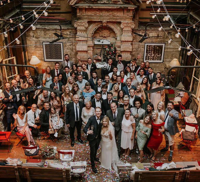 Wedding at Brody Studios in Budapest, Hungary | Bride in Lila Gown by Alexandra Grecco with Fitted Silk Crepe Skirt and Sheer Italian Tulle Bodice Covered in Floral Lace Applique | Theia Bridal Veil with Petal Detail | Groom in Black Three-Piece Suit from Hackett with Burgundy Bow Tie from Zara | Colourful Confetti | Festoon Lights | Budapest Wedding with Giant Bridal Bouquet, Tuk Tuks and Cadillac | Jágity Fanni Fotográfus