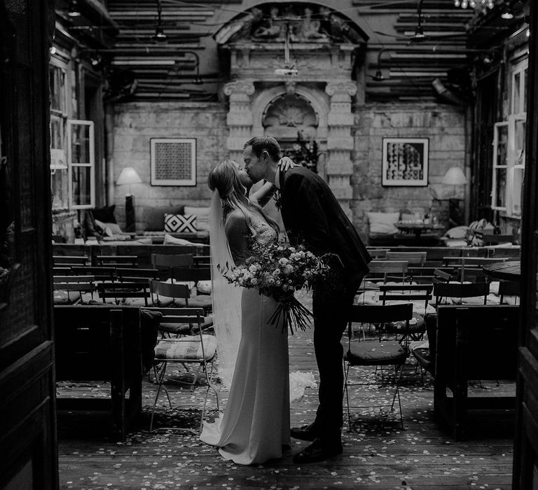 Bride in Lila Gown by Alexandra Grecco with Fitted Silk Crepe Skirt and Sheer Italian Tulle Bodice Covered in Floral Lace Applique | Theia Bridal Veil with Petal Detail | Oversized  Bouquet with Pink, Red and White Flowers and Foliage | Groom in Black Three-Piece Suit from Hackett with Burgundy Bow Tie from Zara | Wedding at Brody Studios in Budapest, Hungary | Budapest Wedding with Giant Bridal Bouquet, Tuk Tuks and Cadillac | Jágity Fanni Fotográfus