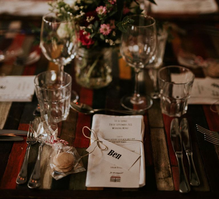 Macaron Wedding Favour | Wedding Breakfast Menu Tied with Twine | Pink, Red and White Flowers in a Jar | Colourful Wooden Table | Wedding Reception at Brody Studios in Budapest, Hungary | Budapest Wedding with Giant Bridal Bouquet, Tuk Tuks and Cadillac | Jágity Fanni Fotográfus